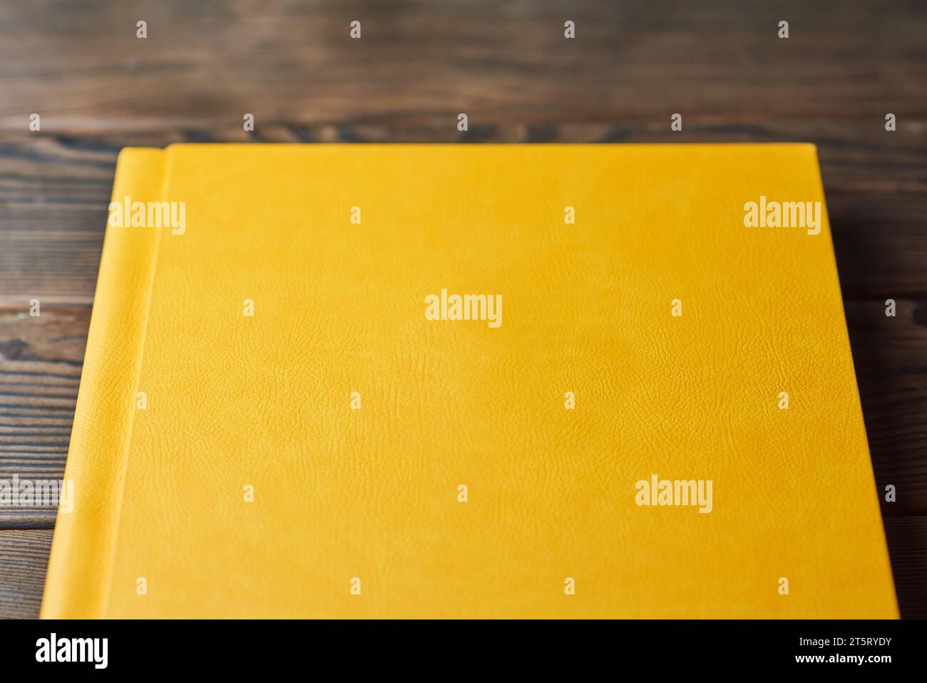 Buch mit gelbem strukturiertem Hardcover auf braunem Holzhintergrund. Perspektivische Ansicht, Nahaufnahme, zugeschnitten. Layout mit leerem Deckel. Konzept von Re Stockfoto