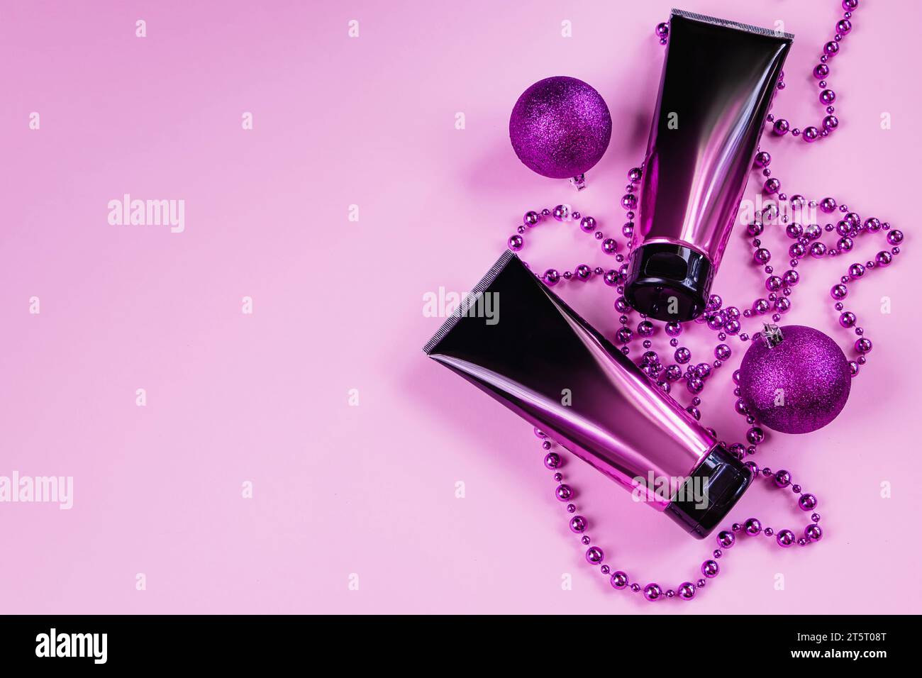 Set aus schwarzen und rosa Squeeze Kosmetikflaschen und lila Dekorationen auf pastellfarbenem Hintergrund. Hautpflege, Lotion oder Creme im luxuriösen Kosmetiktubus. Entkleiden Stockfoto