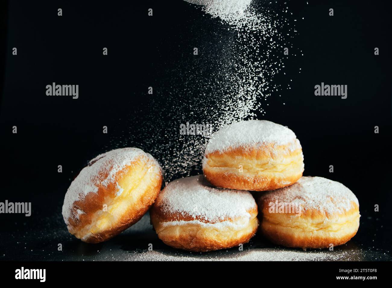 Puderzucker wird auf Donuts gegossen. Traditionelles jüdisches Dessert Sufganiyot auf schwarzem Hintergrund. Wir feiern den Judaismus. Kochen gebratene Berliner. Stockfoto