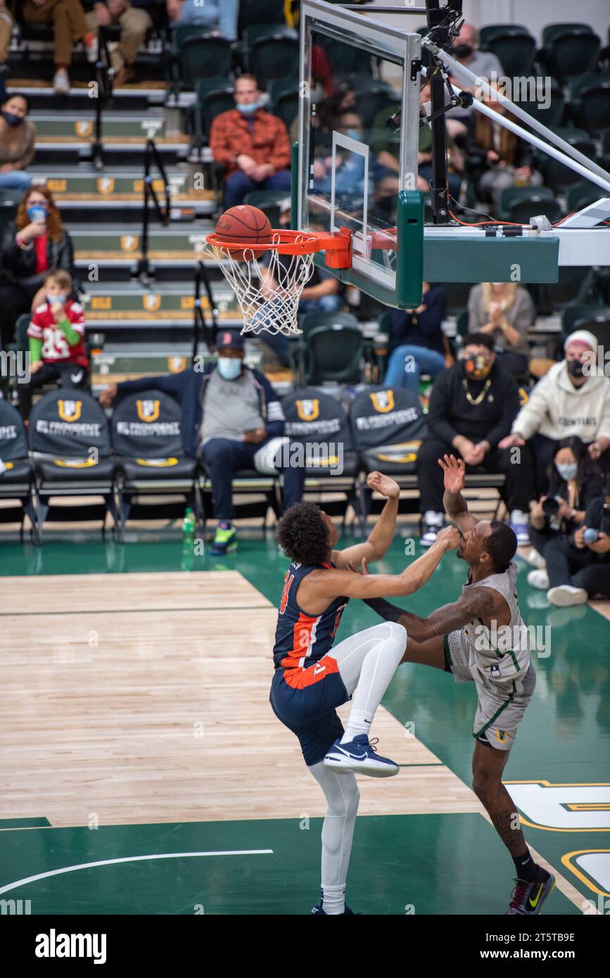 College-Basketballspieler, der einen umstrittenen Layup während der NCAA-Action beendet, aufgenommen mit scharfen Details, starker Körperkontrolle und dynamischen Spielbewegungen Stockfoto