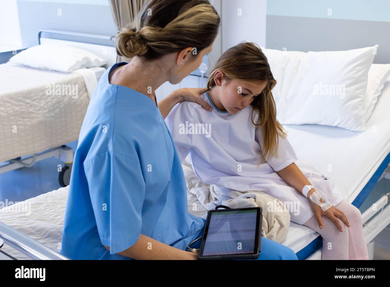 Kaukasische Ärztin mit Tablette tröstet trauriges Mädchen Patientin sitzend auf Krankenhausbett Stockfoto