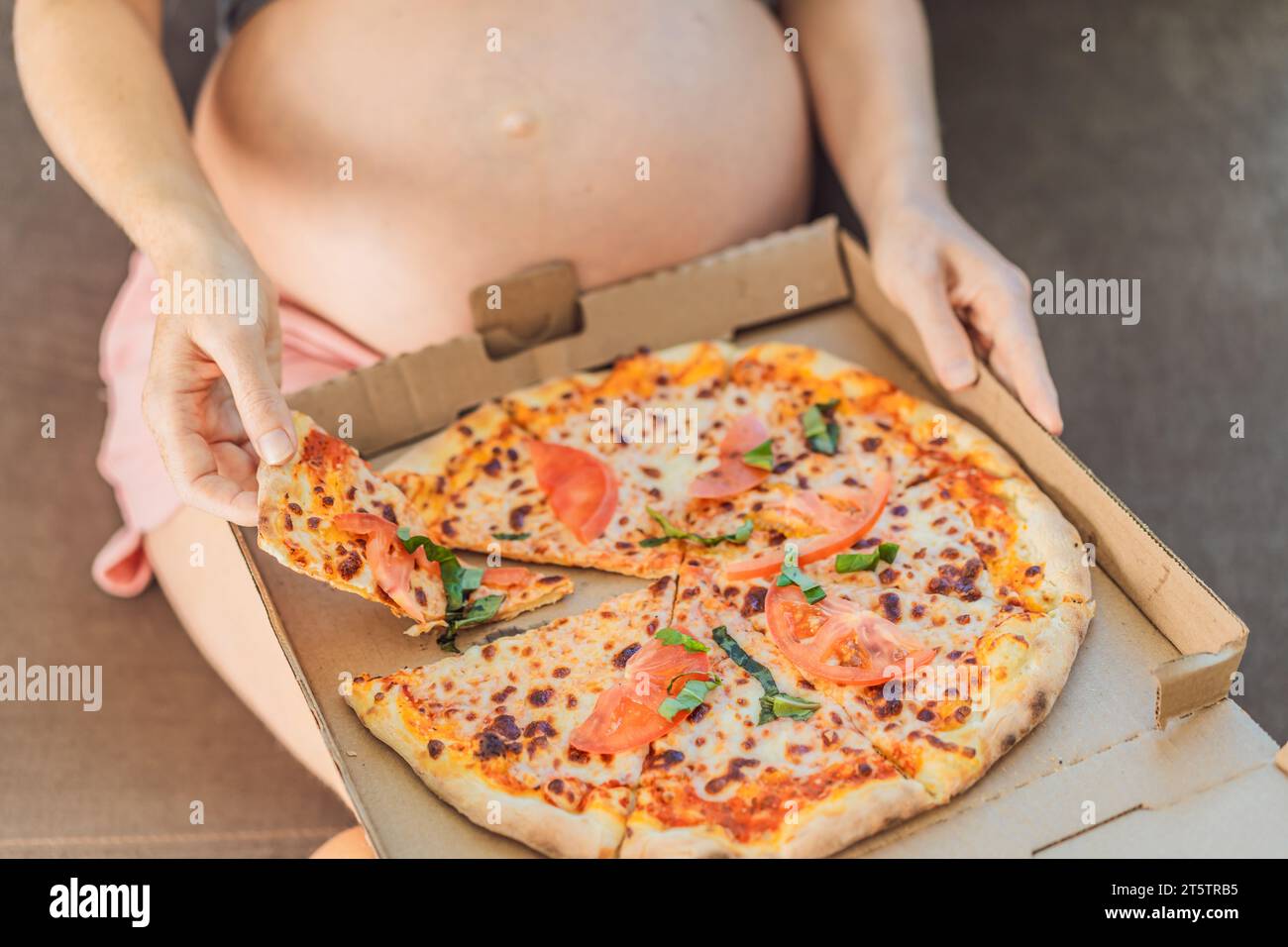 Eine schwangere Frau genießt ein Stück Pizza und genießt einen Moment der Genussfreude, während sie ihr Verlangen nach einer köstlichen, wohltuenden Leckerei befriedigt. Begeistert Stockfoto