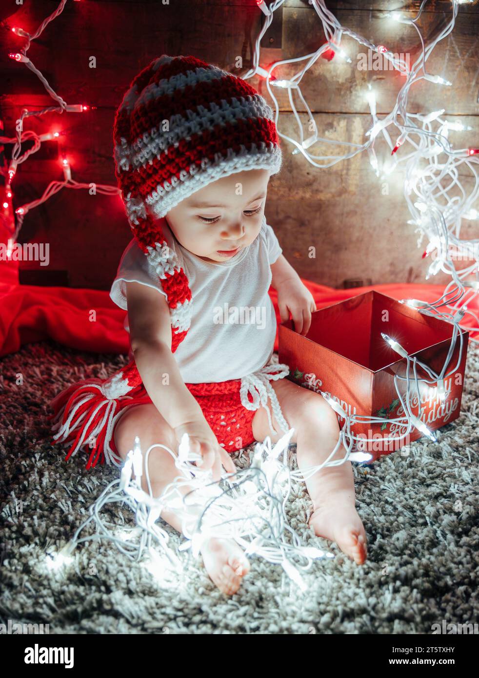 Kind in Strickmütze spielt mit leuchtenden Weihnachtslichtern Stockfoto