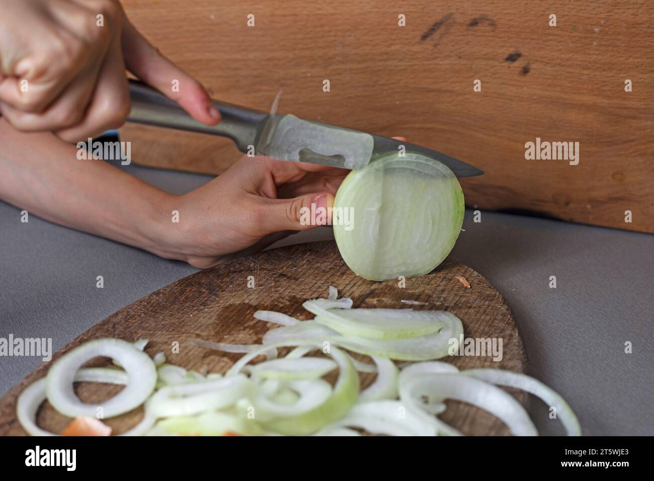 Mädchen schneidet rohe Zwiebeln in Ringe für Gemüsesalat mit einem Messer Stockfoto