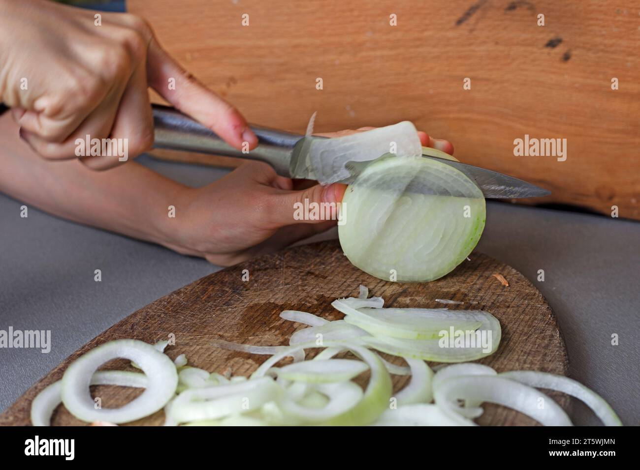 Mädchen schneidet rohe Zwiebeln in Ringe für Gemüsesalat mit einem Messer Stockfoto