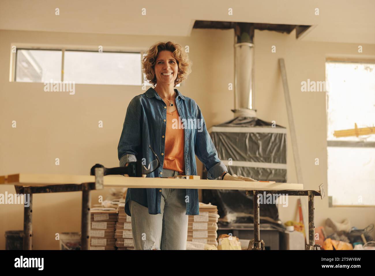 Glückliche weiße Frau mit Schutzbrille renoviert ihr Haus. Sie ist drinnen in der Küche und modernisiert den Raum geschickt mit Holzpaneelen und Stockfoto