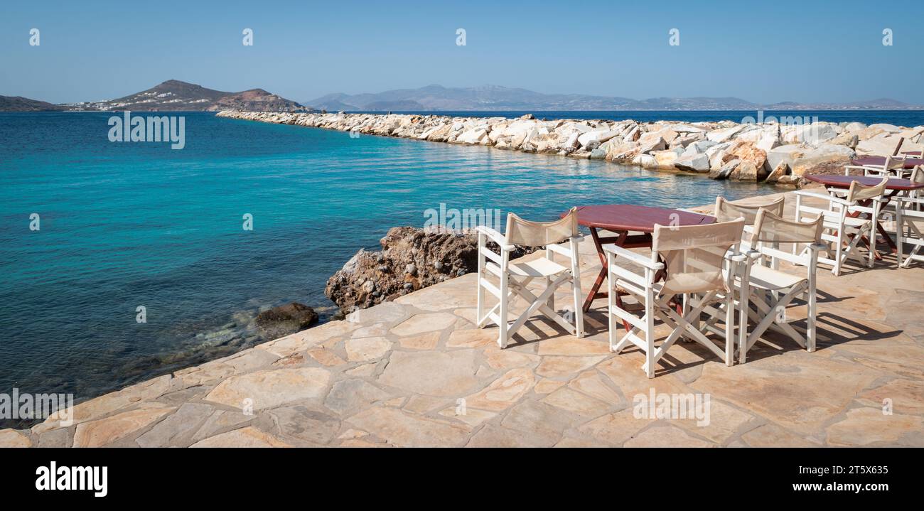 Naxos Griechenland Panoramablick mit Tischen und Stühlen entlang des Meeres und Wellenbrechers in der Nähe des Hafens von Naxos Island. Stockfoto