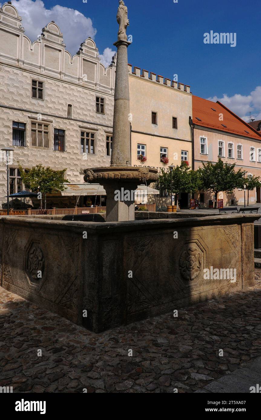 Brunnen in Míru náměstí (Friedensplatz) in Slawonien, Südböhmen, Tschechien. Der Brunnen zeigt eine toskanische Säule aus den späten 1600er Jahren eines ehemaligen Prangers, auf der eine Marienstatue aus den späten 1700er Jahren zu sehen ist. Die Basis des Brunnens ist ein quadratisches Steinbecken aus den 1500er Jahren, das mit dem fünfblättrigen Rosenemblem der Familie Vítkovec, Herren von Hradec, verziert ist. Míru náměstí hat viele schöne Häuser mit Renaissancefassaden, die mit Sgraffito verziert sind. Stockfoto