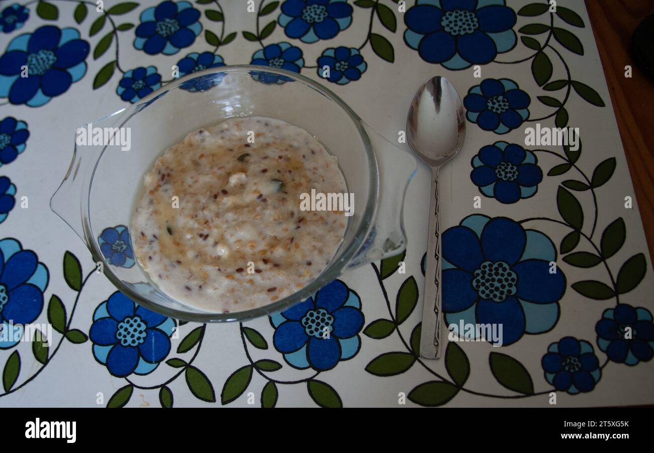 Schüssel mit dampfendem Brei mit Salatstreusel mit Samen und Nüssen und einem Honig, der auf einem blauen Tischset steht Stockfoto