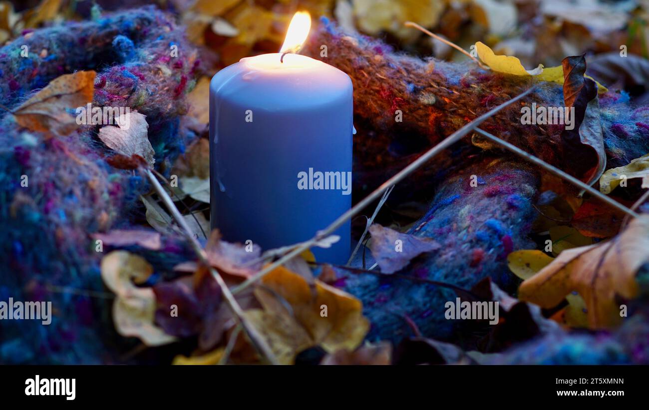 Eine blaue Kerze zwischen Herbstblättern - ein Schal um sie herum. Stockfoto