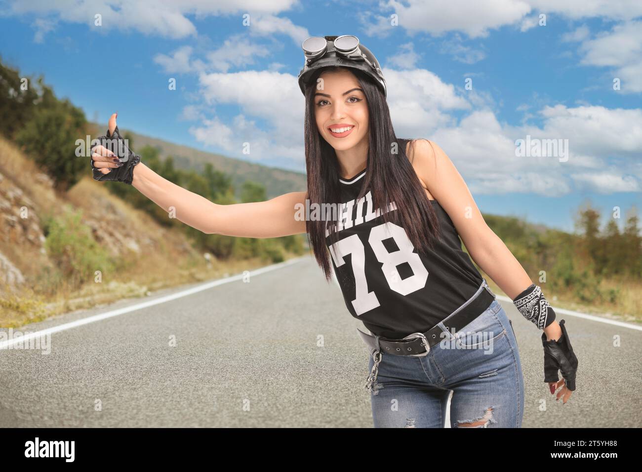 Junge Radfahrerin mit Helm und Schutzbrille per Anhalter auf offener Straße Stockfoto