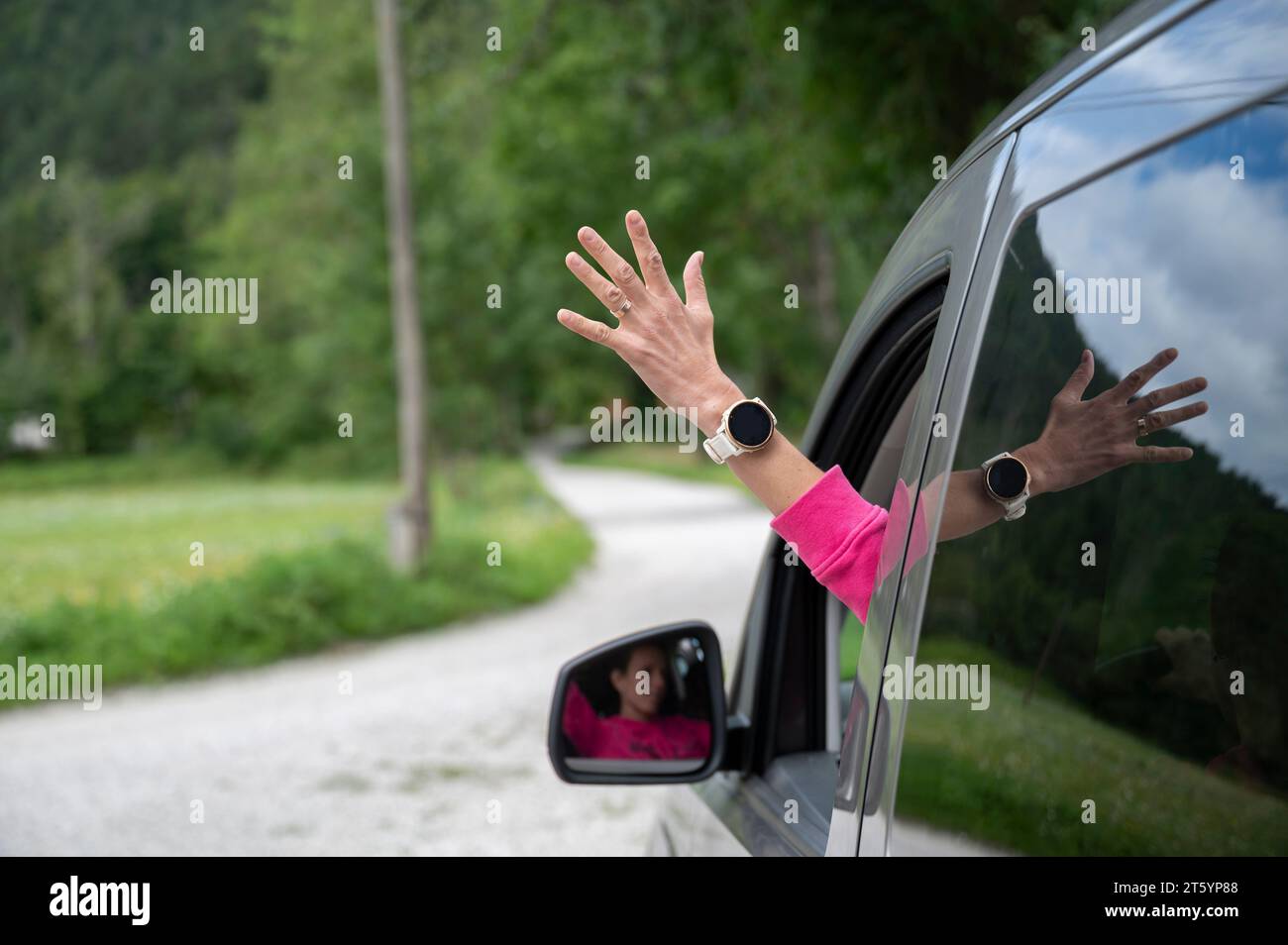 Weibliche Hand, die aus einem Fenster eines fahrenden Fahrzeugs ragt, eines Autos, auf einer Schotterstraße. Stockfoto