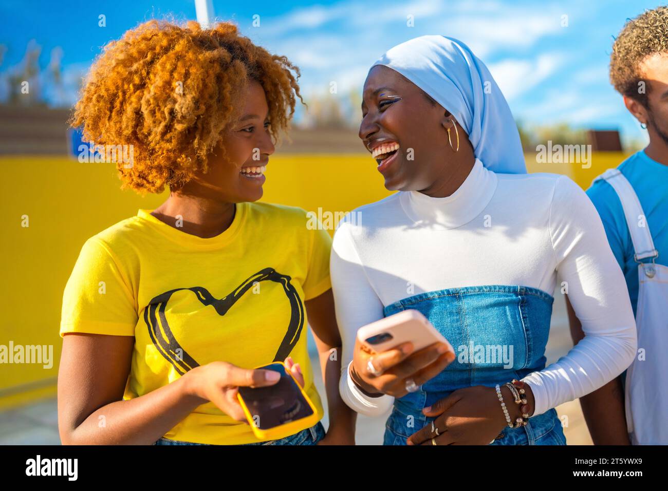 Frontal glückliches Porträt zweier junger afroamerikanischer Frauen, die draußen telefonieren Stockfoto