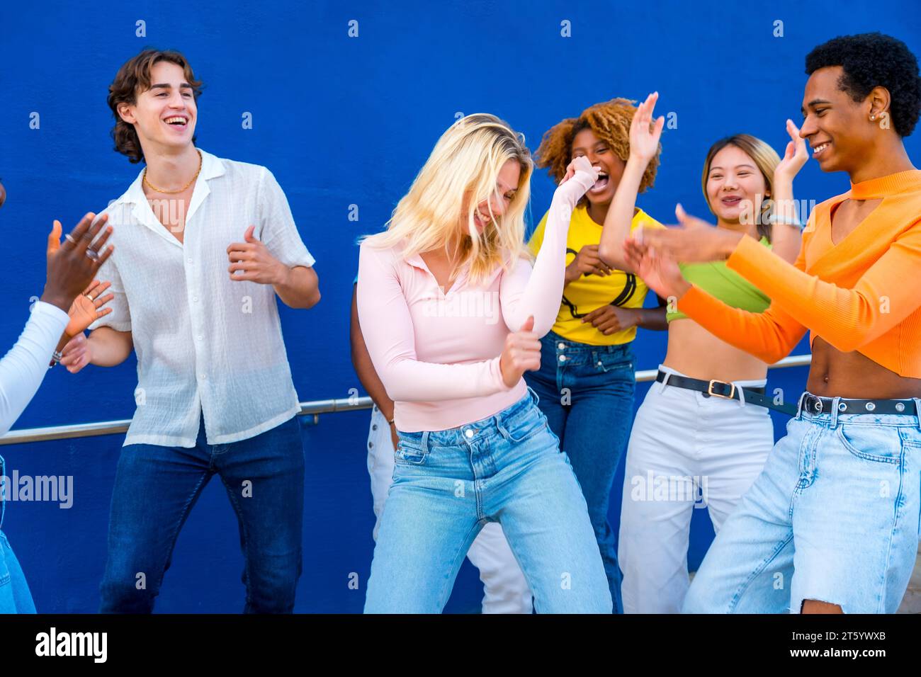 Blonde junge Frau tanzt in einer Tanzschlacht mit Freunden mit einer blauen Wand als Hintergrund Stockfoto