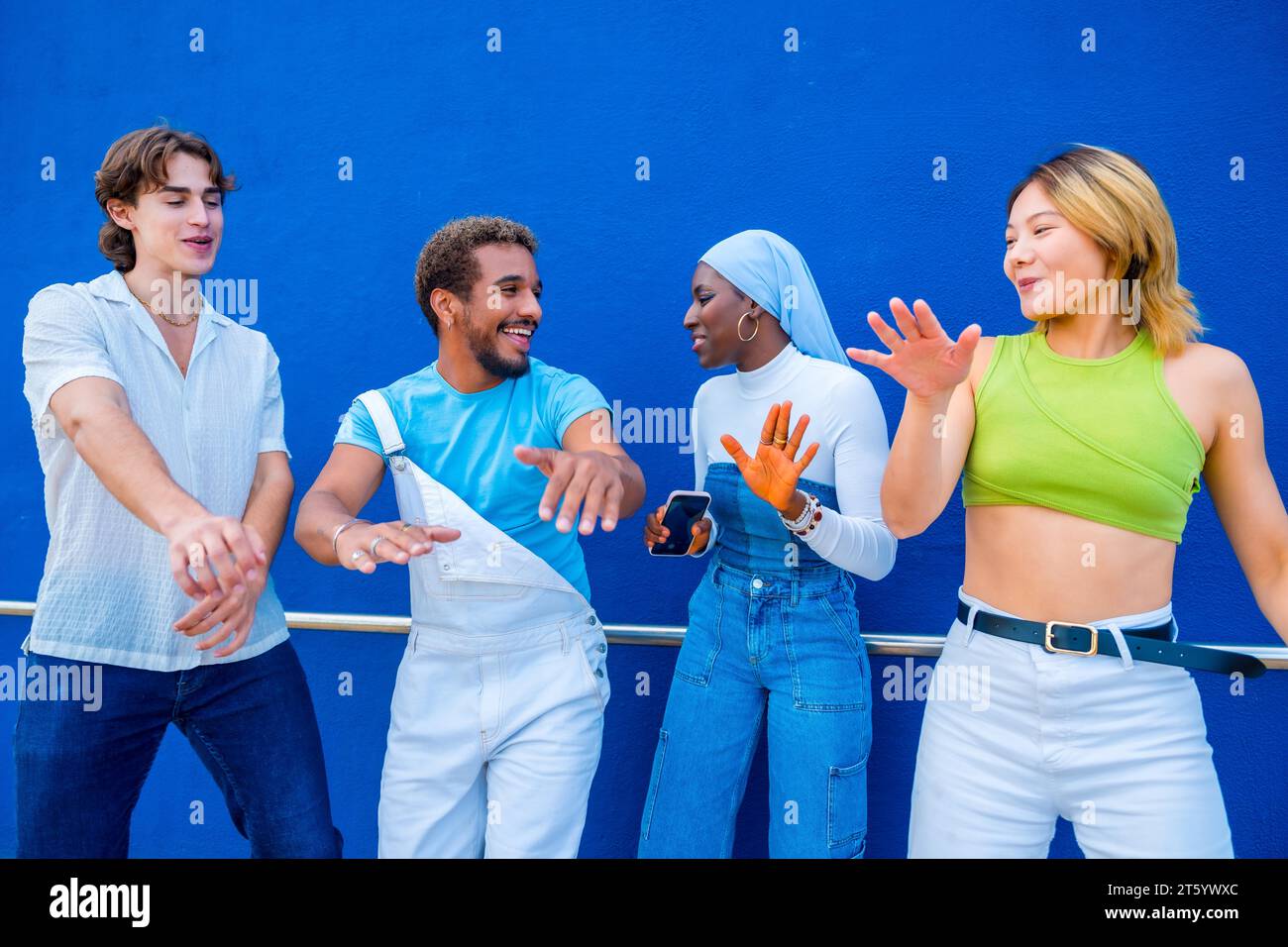 Multikulturelle Jugendliche tanzen eine musikalische Choreographie in einem blauen urbanen Raum Stockfoto