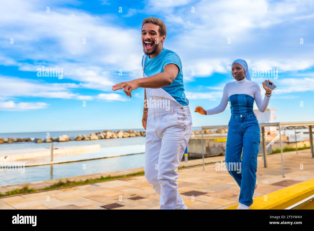 Seitenansicht von zwei fröhlichen, multiethnischen Freunden, die am Meer tanzen Stockfoto