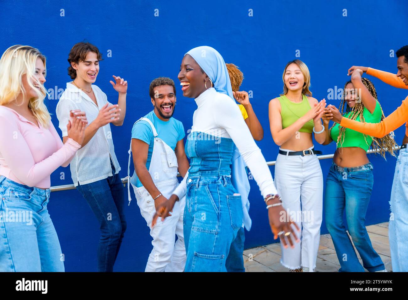 Muslimische junge Frau tanzt in einer Tanzschlacht mit Freunden mit einer blauen Wand als Hintergrund Stockfoto