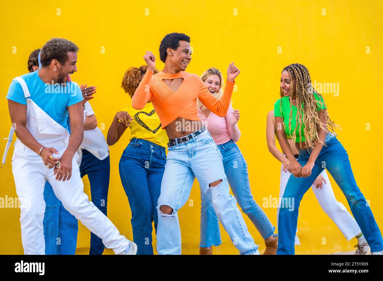 Junge Gruppe von Menschen, die gemeinsam in Koordination auf der Straße vor gelbem Hintergrund tanzen Stockfoto
