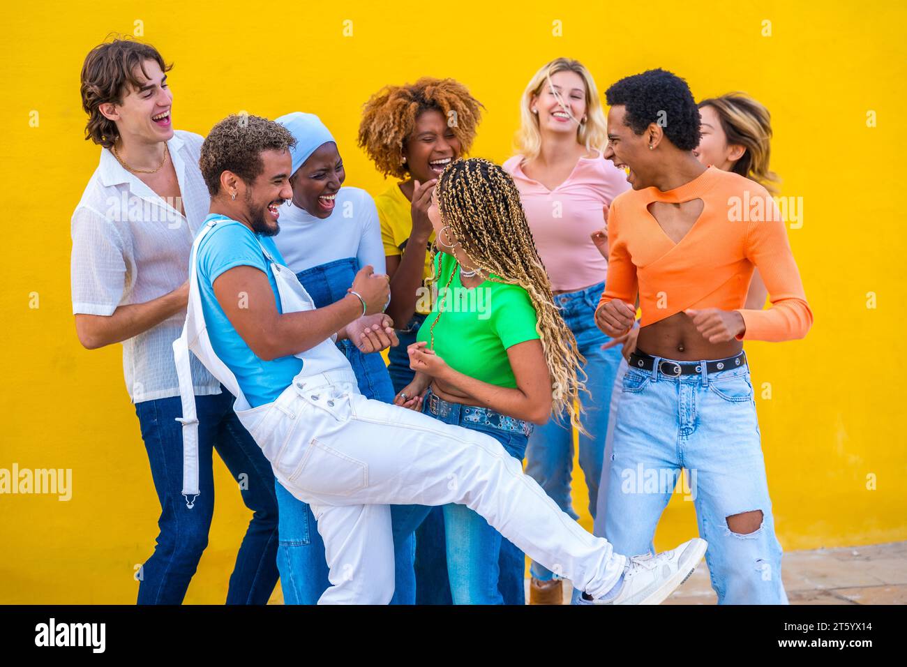 Fröhliche multikulturelle Freunde tanzen und Spaß haben neben einer gelben Wand im Freien Stockfoto
