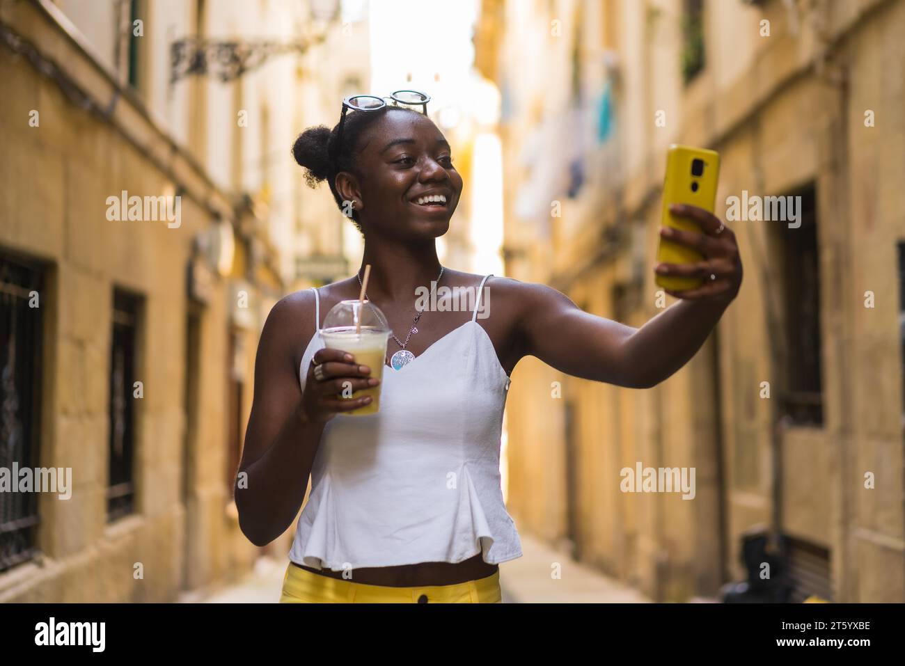 Lächelnde junge afroamerikanerin, die Selfie spricht und einen köstlichen Milchshake in der Stadtstraße zeigt Stockfoto