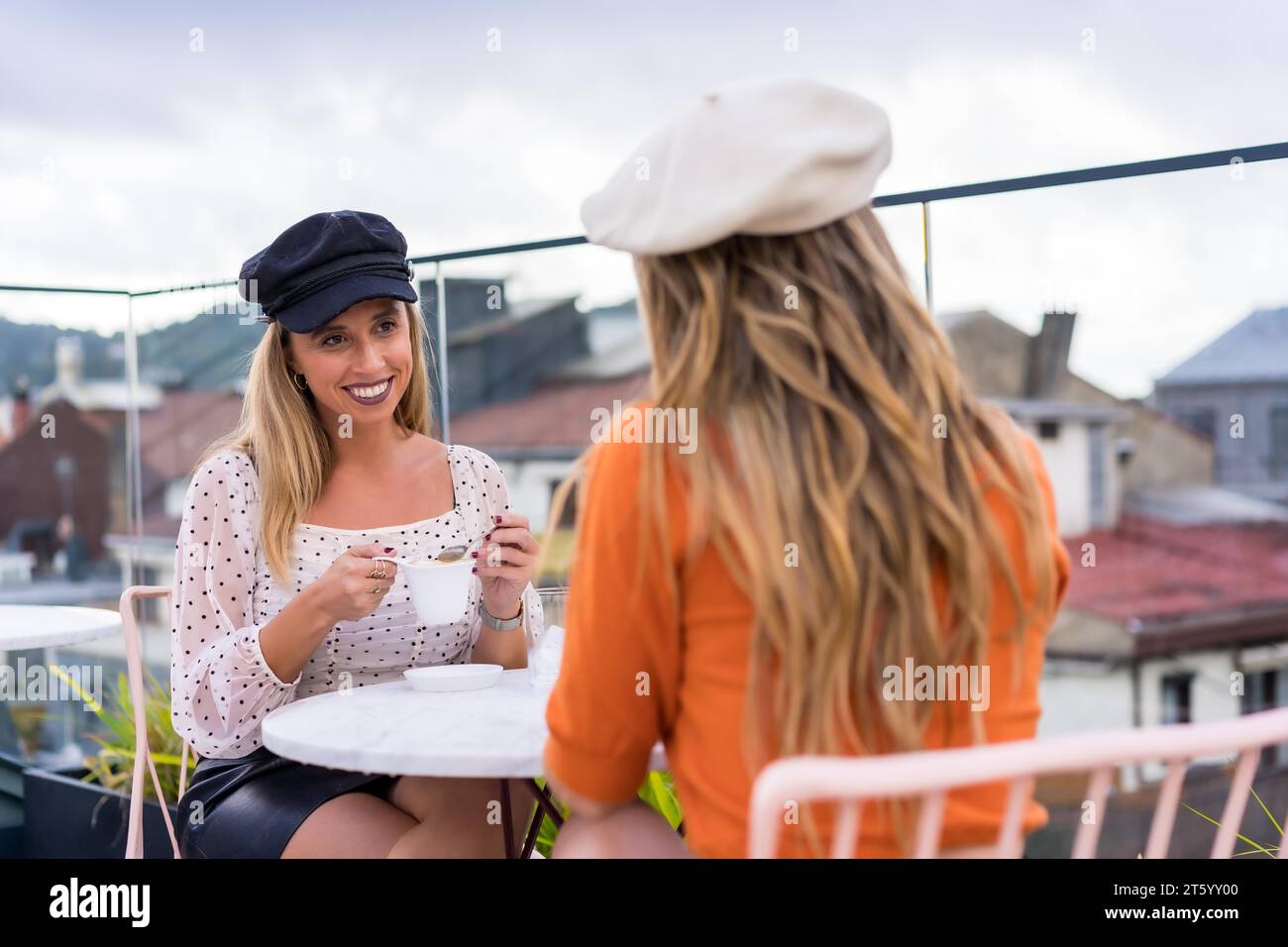 Zwei junge Schönheitsfrauen trinken Kaffee auf einer Außenterrasse mit Blick auf die Stadt Stockfoto