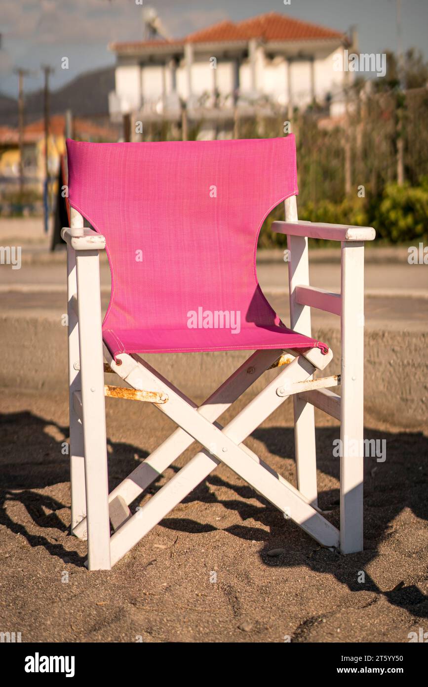 Ein einsamer pinkfarbener Canvas-Sessel sitzt verlassen an einem ruhigen griechischen Strand, der im goldenen Licht der untergehenden Sonne getaucht ist und einen friedlichen Ort für conte bietet Stockfoto