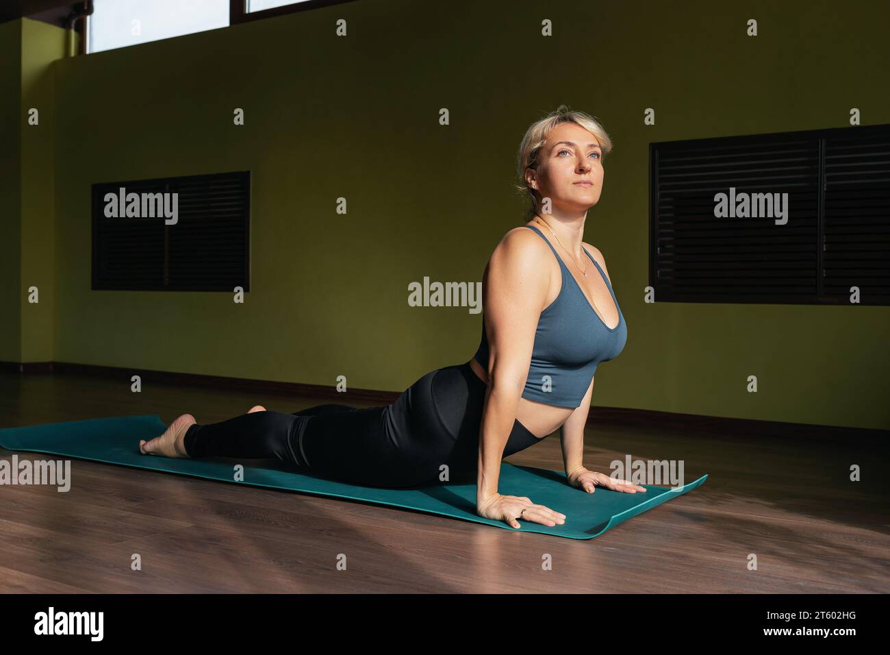 Athletische blonde Frau, die Yoga übt, Übung Adho mukha shvanasana durchführt, nach oben gerichtete Hundestellung, Training in Sportbekleidung auf einer Matte in einer Fitness Stockfoto
