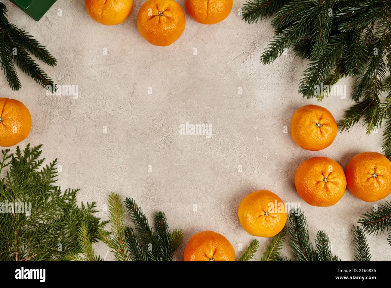 Weihnachtsrahmen mit süßen Mandarinen in der Nähe von wacholder und Tannenzweigen auf grauer strukturierter Oberfläche Stockfoto