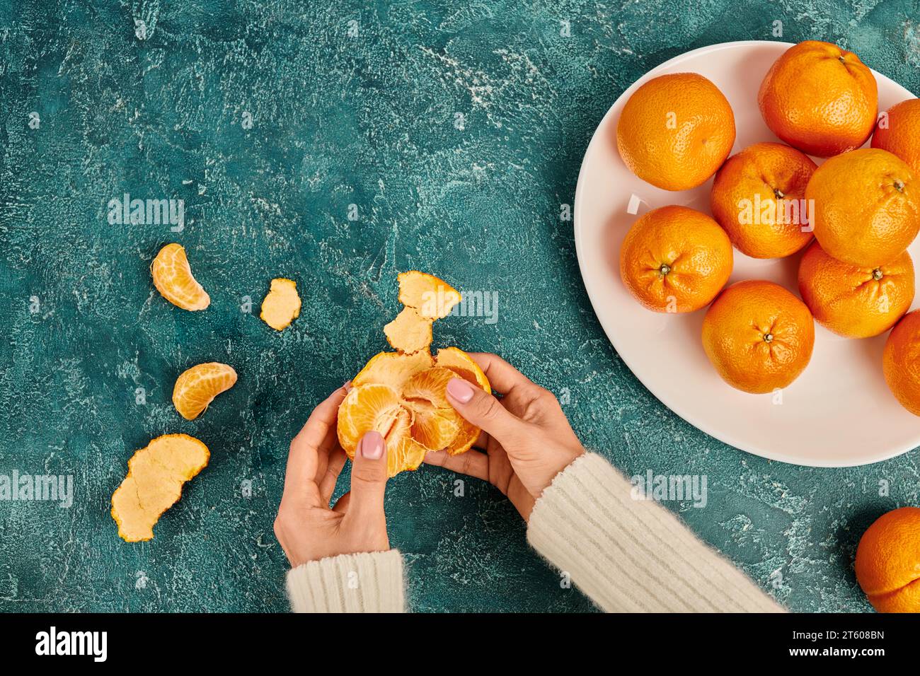Zugeschnittene Ansicht einer Frau, die frische und süße Mandarine vor blauem Hintergrund schält, Weihnachtskonzept Stockfoto