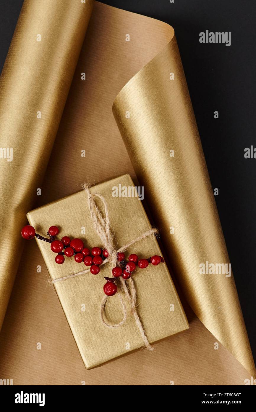 goldene Geschenkbox mit roten stechpalmenbeeren auf glänzendem Geschenkpapier und schwarzem Hintergrund, Weihnachtsdekor Stockfoto