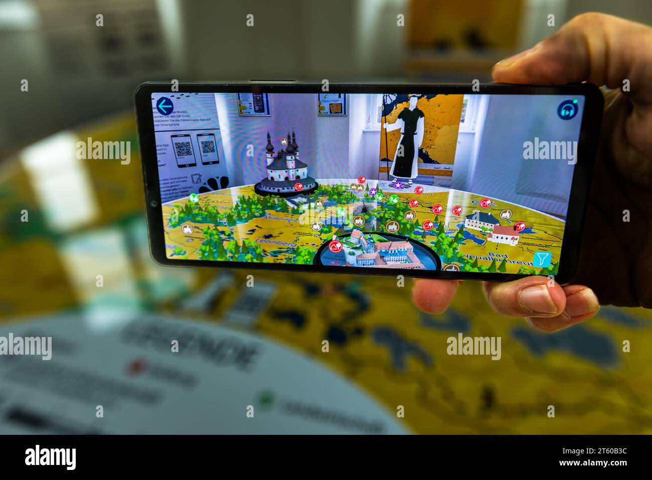 Eine Hand hält ein Smartphone, dessen Bildschirm die App Cisterscapes zeigt, die ein 3D-Modell der Landschaft Waldsassen anzeigt und die Orte markiert, an denen die Zisterziensermönche einst arbeiteten. Waldsassen, Bayern, Deutschland. Stockfoto