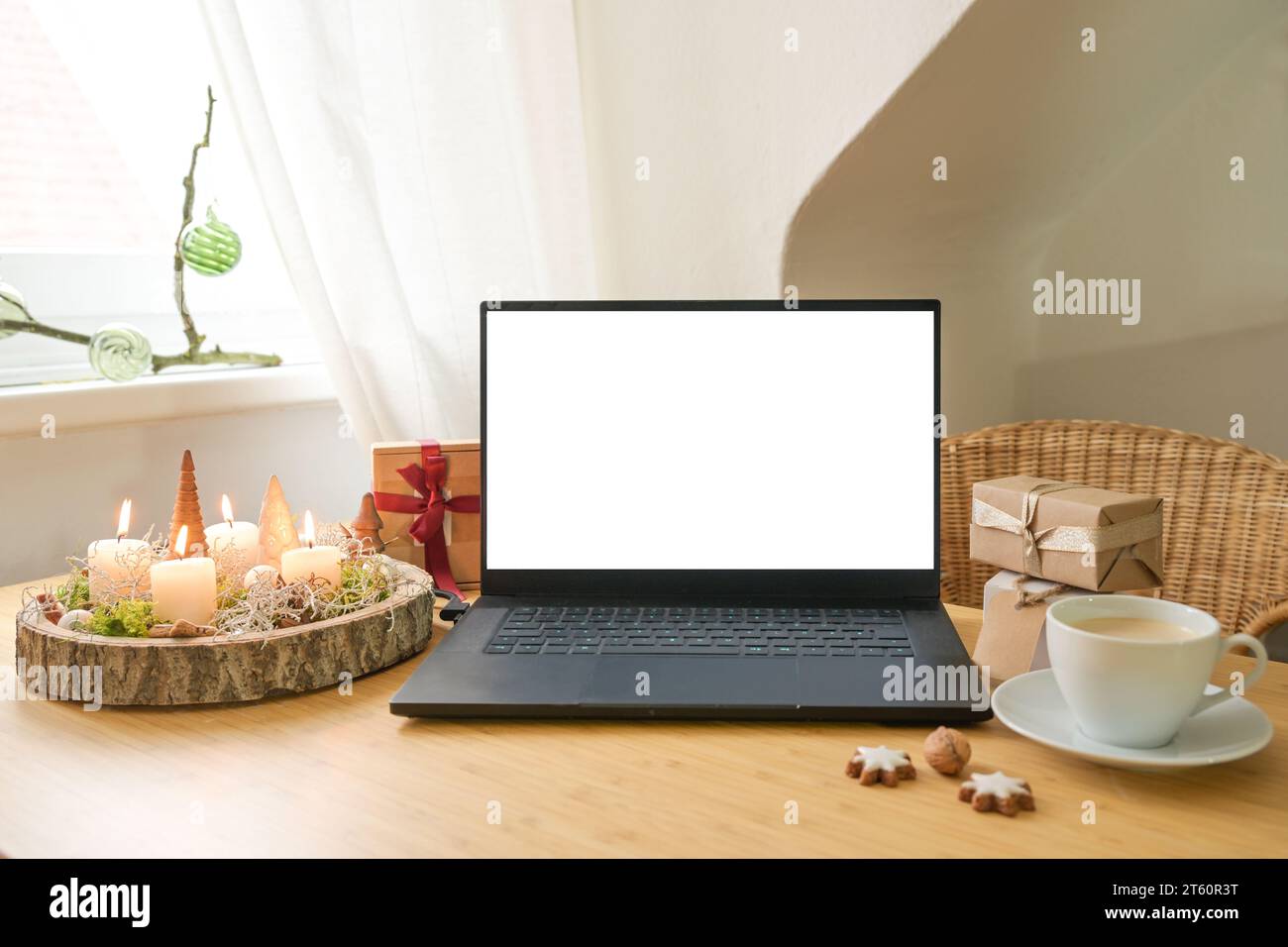 Mockup eines weißen Laptop-Bildschirms auf einem Holzschreibtisch mit Geschenken, Adventskerzen und Weihnachtsdekoration in einer Dachwohnung, Urlaub Online Shopping, c Stockfoto