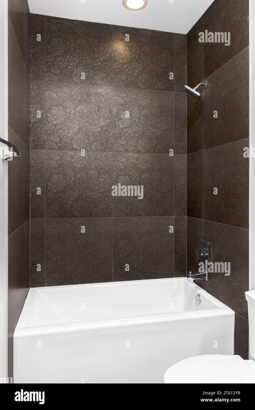 Eine Dusche mit braunen Fliesen und Paisley-Blumenmustern, weiße Badewanne und polierte Chromarmaturen. Stockfoto