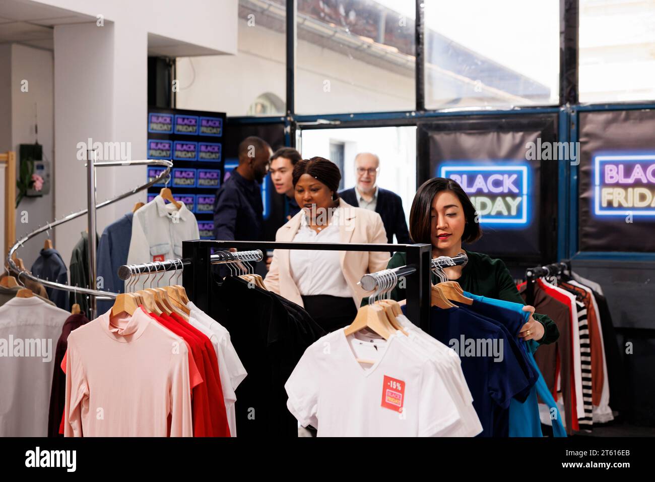 Einkaufssaison. Der Sicherheitsbeamte eröffnet am Black Friday einen Bekleidungsladen und lässt Kunden rein. Begeistert waren die verschiedensten Kunden, die impulsive Einkäufe tätigen und Kleidung zu Discountpreisen kauften Stockfoto