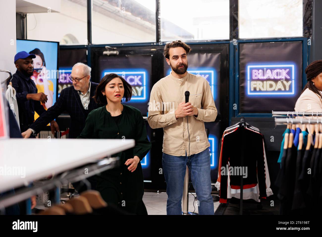 Verrückte, besessene Leute, die sich um Deals in den Laden bewerben, vorbei an Reportern, die Live-Übertragungen über Black Friday-Einkäufe übertragen haben. TV-Korrespondent berichtet Live-Nachrichten aus einem Modegeschäft während der saisonalen Verkäufe Stockfoto