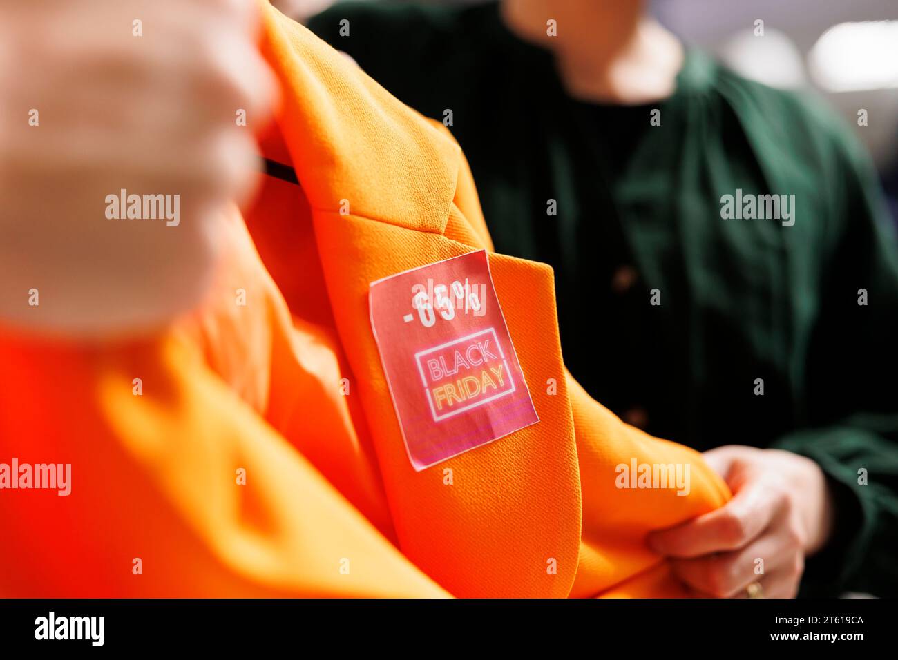 Black Friday Fashion Deals. Nahaufnahme des roten Rabattschilds auf Kleidungsstück. Während der saisonalen Verkaufszeiten kaufen die Leute Kleidung zu ermäßigten Preisen im Einkaufszentrum, die Käufer kämpfen um einen orangefarbenen Blazer Stockfoto