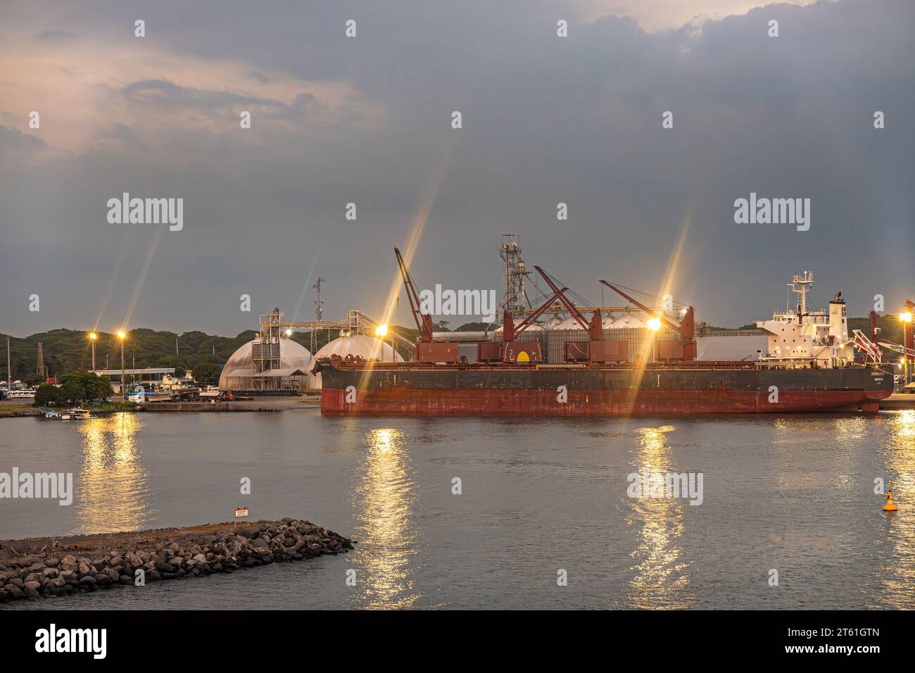 Guatemala, Puerto Quetzal - 20. Juli 2023: Abendliche Wolkenlandschaft. Sonnenuntergang Reflexionen auf Hafenlichtern rund um den Kohlefrachter Unity Endeavour Stockfoto