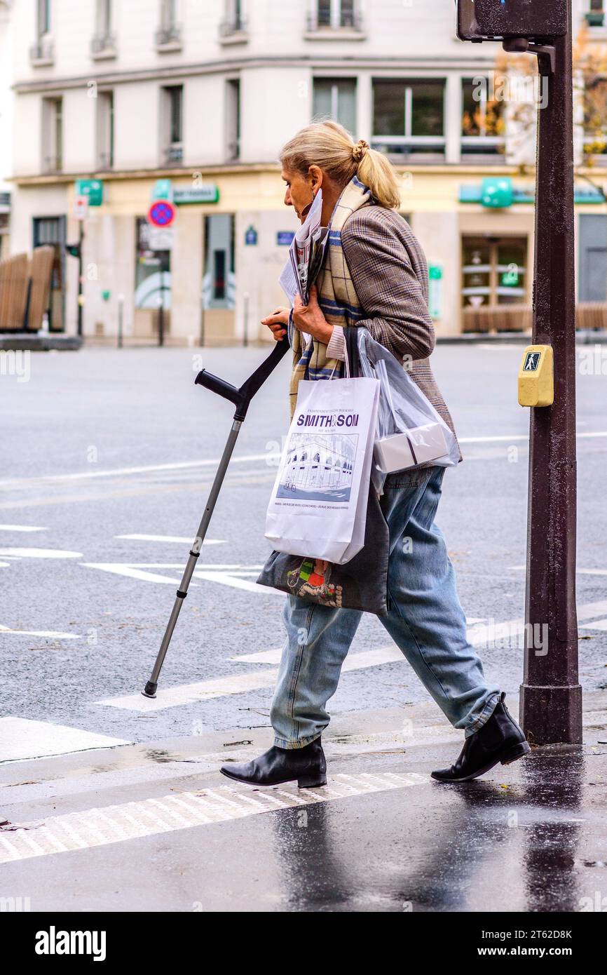 Gut gekleidete Frau mit medizinischem Gehstock am Straßenübergang im Stadtzentrum - Paris 20, Frankreich. Stockfoto