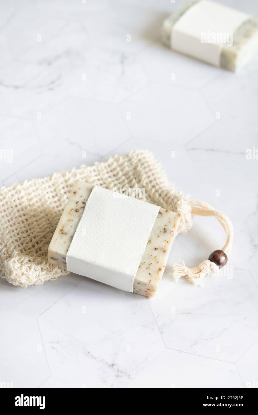 Beige handgemachte Seifenriegel mit leerem Etikett auf Sisal Seifensparbeutel auf Marmortisch Nahaufnahme, Modell, Kopierraum. Natürliche pflanzliche Produkte für Gesicht und b Stockfoto