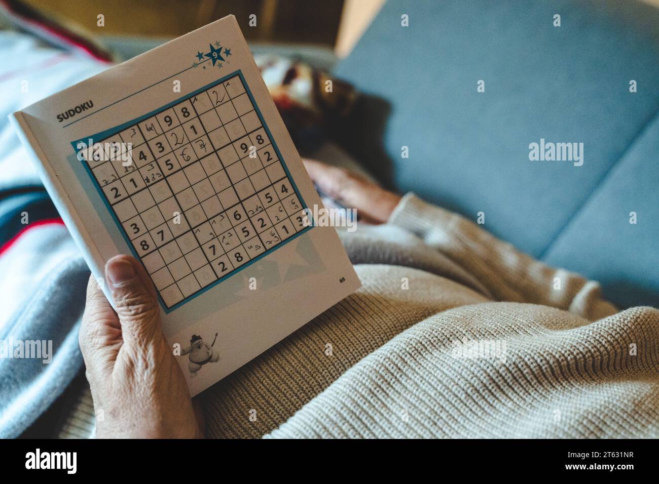 Augsburg, Bayern, Deutschland - 27. Oktober 2023: Eine alte Frau liegt auf einem Sofa im Wohnzimmer und spielt Sudoku in einem Buch mit einem Stift *** eine alte Frau liegt auf einem Sofa im Wohnzimmer und spielt Sudoku in einem Buch mit einem Stift Credit: Imago/Alamy Live News Stockfoto