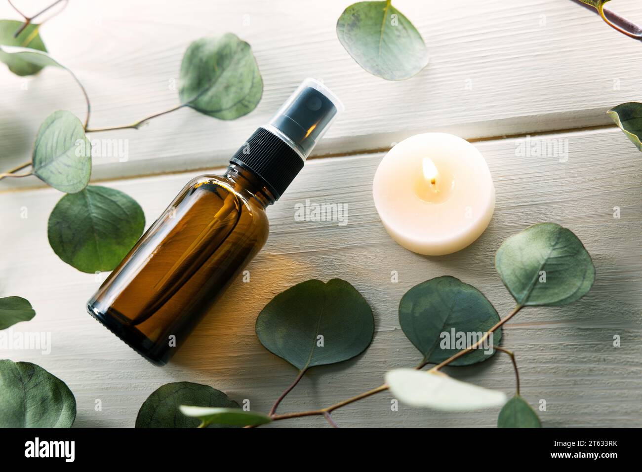 Leere Parfüm-Sprühflasche mit Eukalyptusblättern und Kerze auf weißem Holztisch Stockfoto