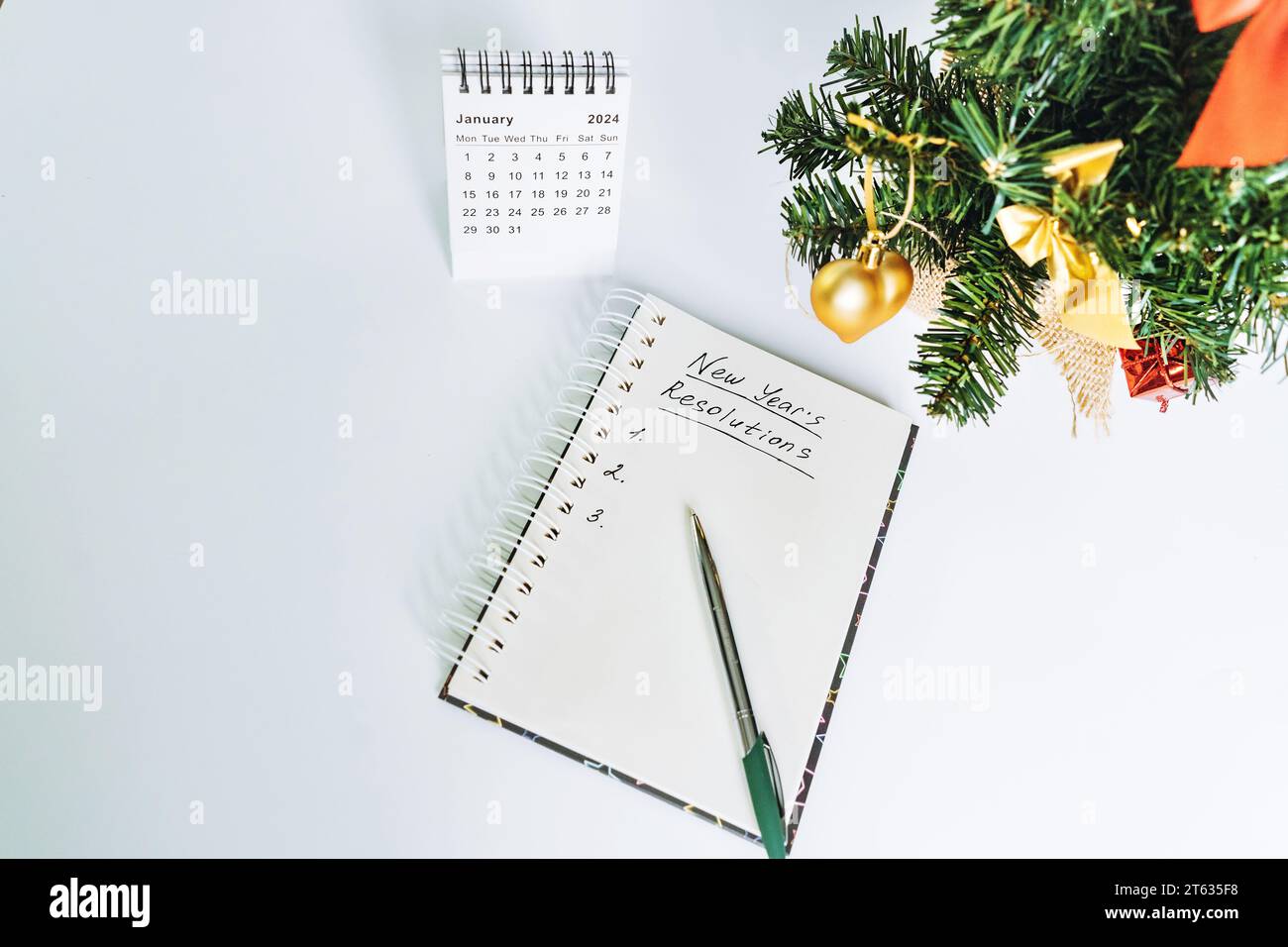 Öffnen Sie den Notizblock mit dem Text „Neujahrsauflösungen“. Januar-Kalender und dekorierter weihnachtsbaum auf Hintergrund Stockfoto