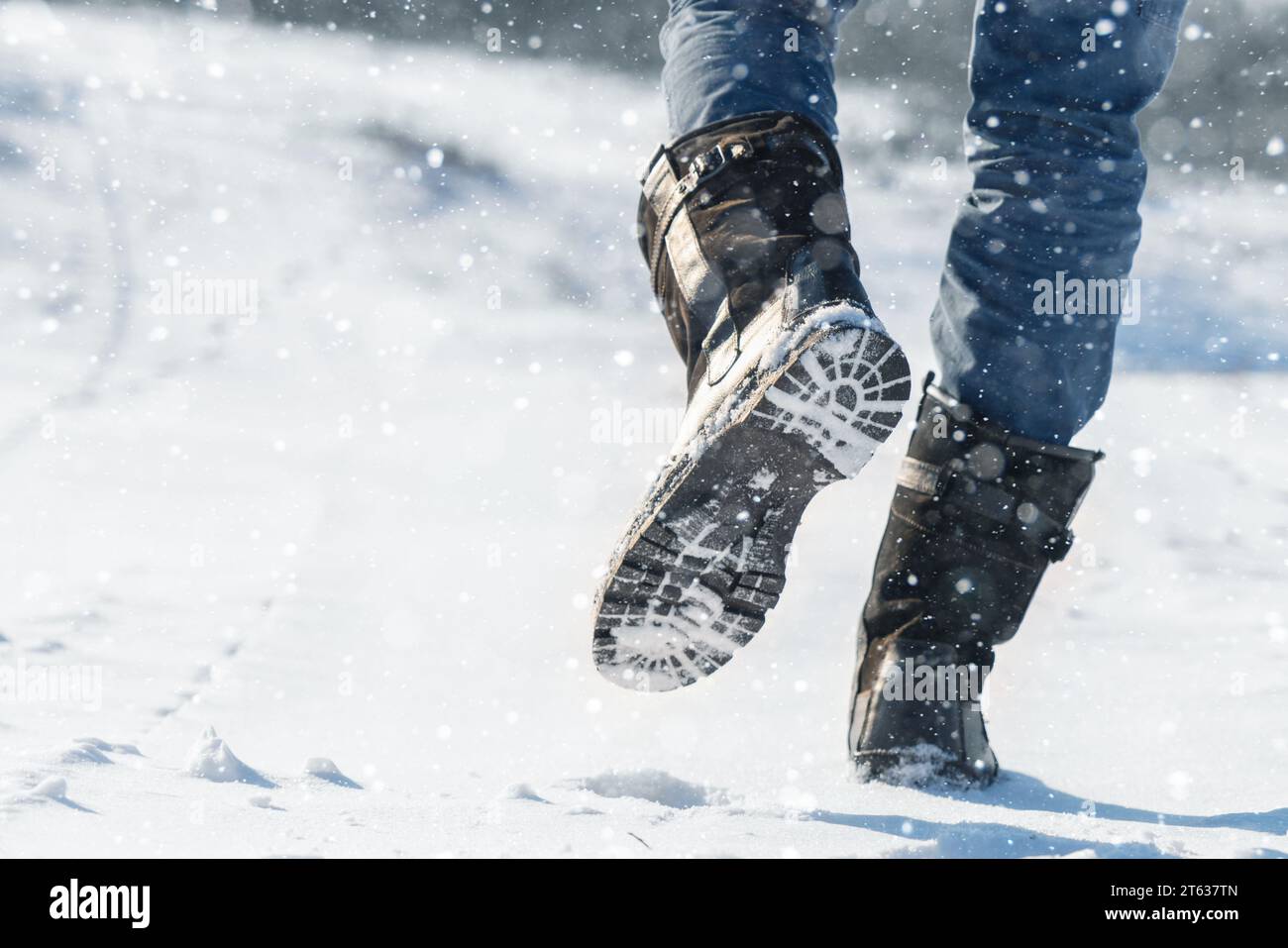 Ein Reisender in Stiefeln spaziert auf einer verschneiten Winterstraße. Stockfoto