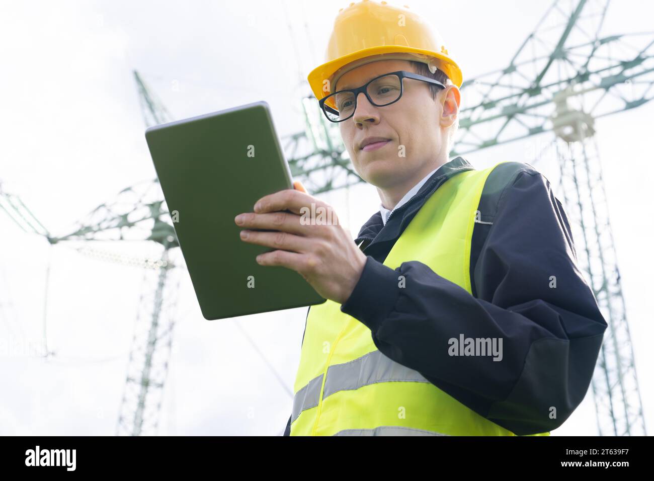Ingenieur mit digitalem Tablet auf dem Hintergrund eines Stromleitungsturms. Stockfoto