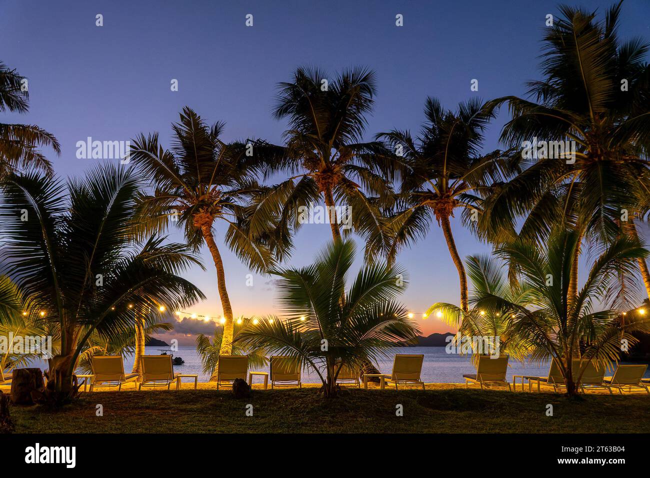 Beleuchtete Palmen und Liegestühle bei Nacht auf Praslin Island, Seychellen Stockfoto