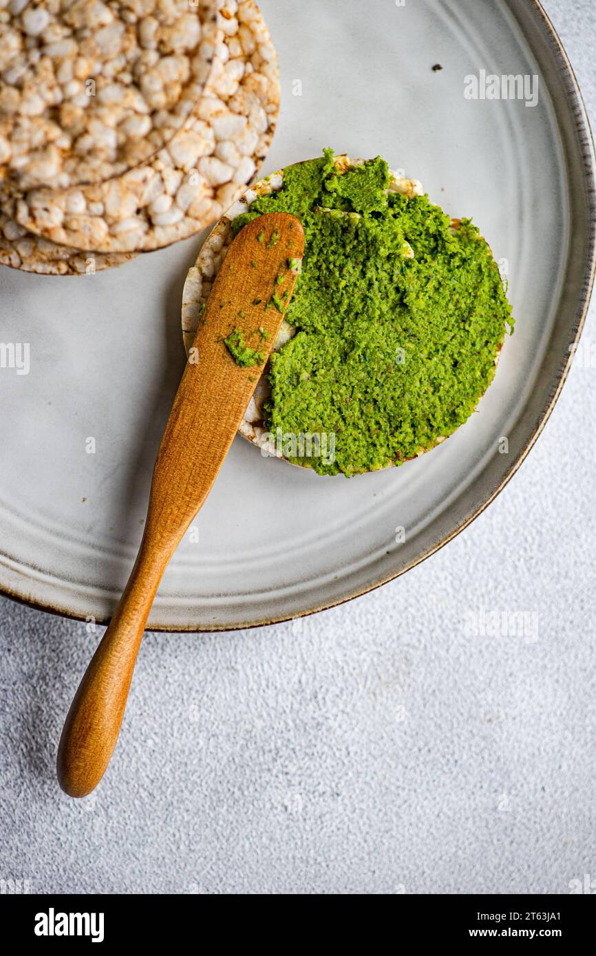 Blick von oben auf Reisbrot auf einem Teller mit leuchtend grünem Spinat-Pesto-Pastasauce vor grauem Hintergrund Stockfoto