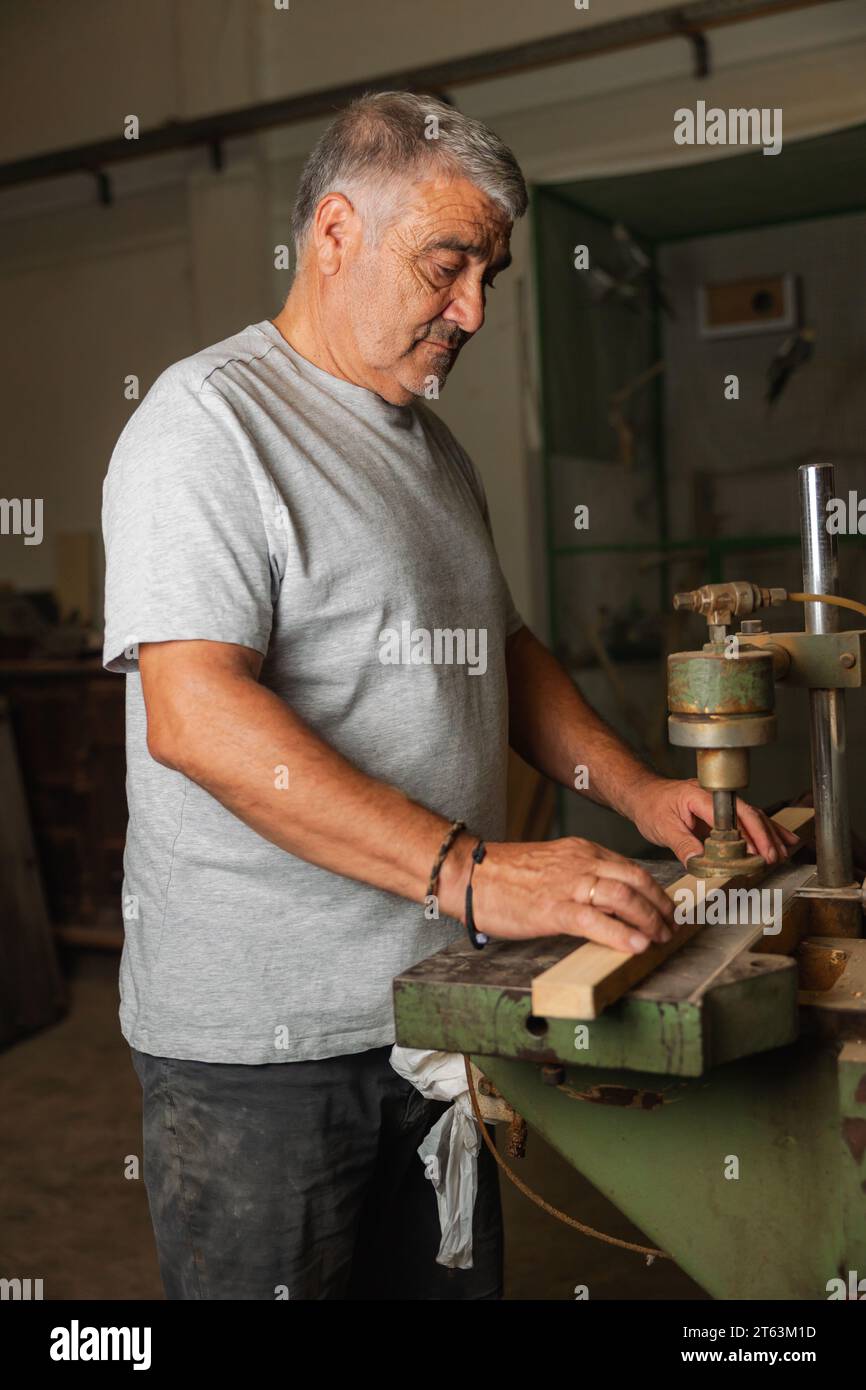Seitenansicht Senior Mann, der fleißig an einem Stück Holz mit Maschinen in einer Tischlerei in Toledo arbeitet Stockfoto