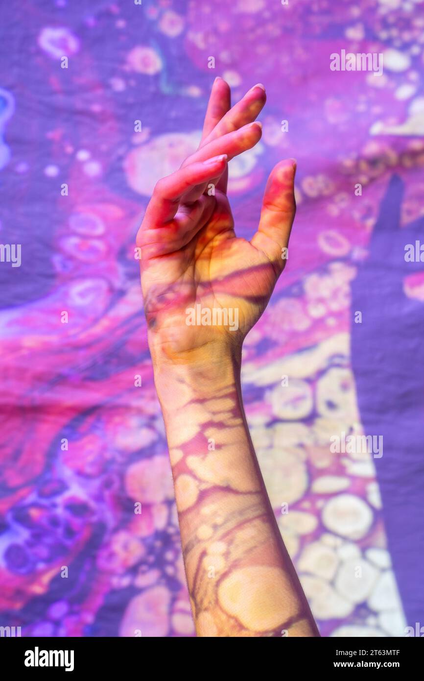 Eine bemalte Hand streckt sich aus und zeigt eine friedliche Geste inmitten eines Reiches von wirbelnden kosmischen Mustern, die spirituelle Erleuchtung und geistige Gesundheit repräsentieren Stockfoto