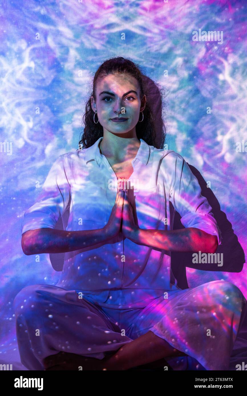 Eine Frau in betender Meditation strahlt eine ruhige Energie gegen eine kosmische Umgebung aus und verkörpert die vereinigung von Spiritualität und geistigem Wohlbefinden Stockfoto