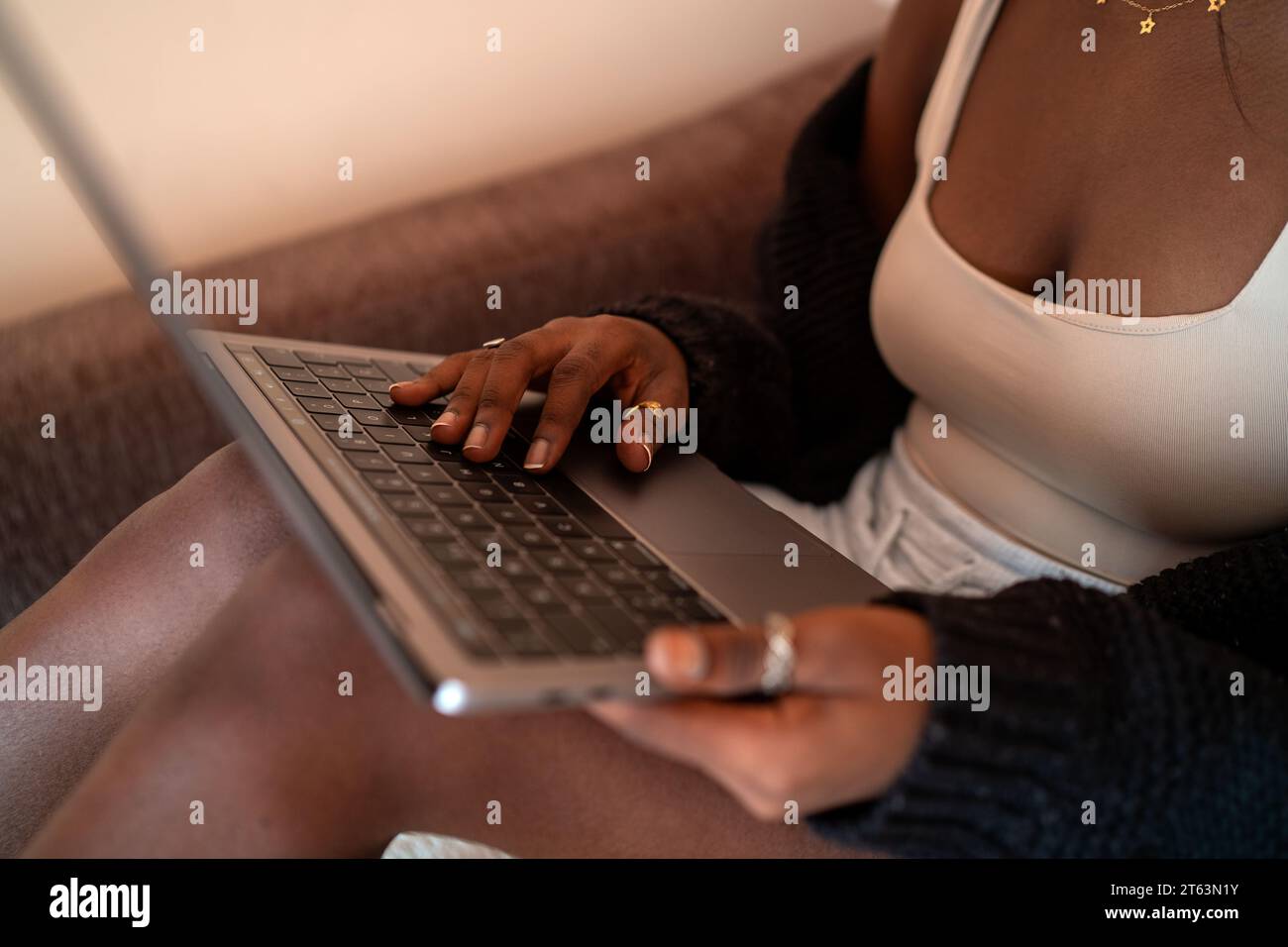 Nahaufnahme einer anonymen afrikanischen Frauenhände, die auf einem Laptop ihren goldenen Ring vor einem weichen Hintergrund ihrer entspannten Kleidung und warmen Raumambia eintippen Stockfoto